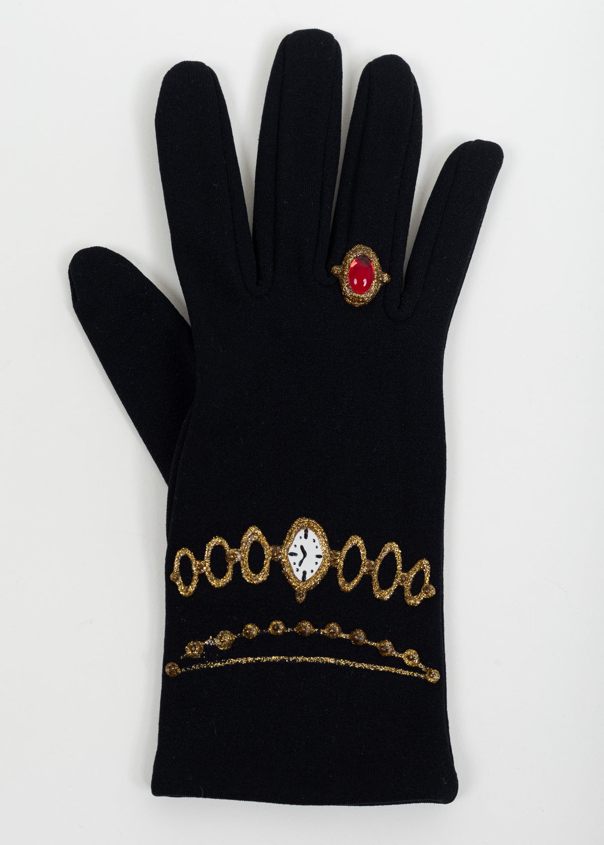 Back of one black glove with a painted white watch face on a gold link bracelet, a beaded gold chain and a red cabochon ring