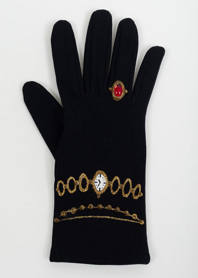 Back of one black glove with a painted white watch face on a gold link bracelet, a beaded gold chain and a red cabochon ring
