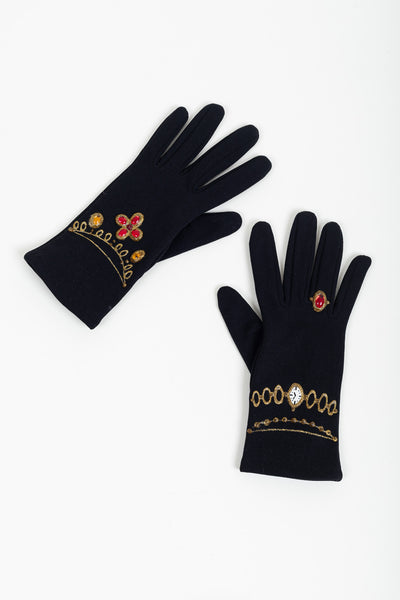 Pair of black evening gloves laid diagonally, one showing the jeweled quatrefoil, the other the painted watch and ring