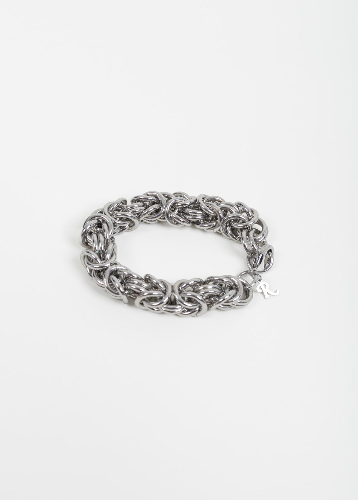 Raf Simons cluster chain bracelet laid flat on white, showing the interlocking silver-tone rings and the R charm at the clasp