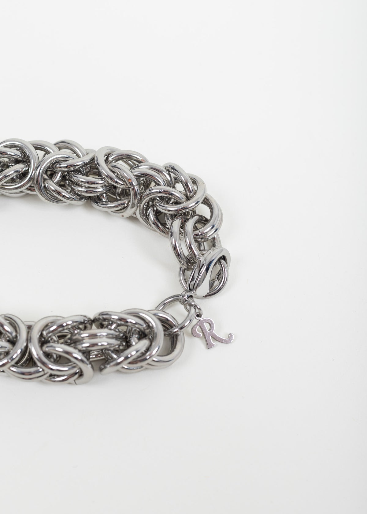 Close-up of the clasp end with lobster clasp and script R charm; small spots of exposed brass are visible on links at the upper left