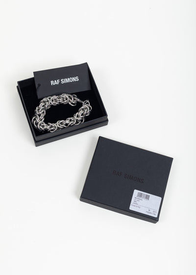 Bracelet in its open black Raf Simons box with brand card, the lid beside it showing the product label
