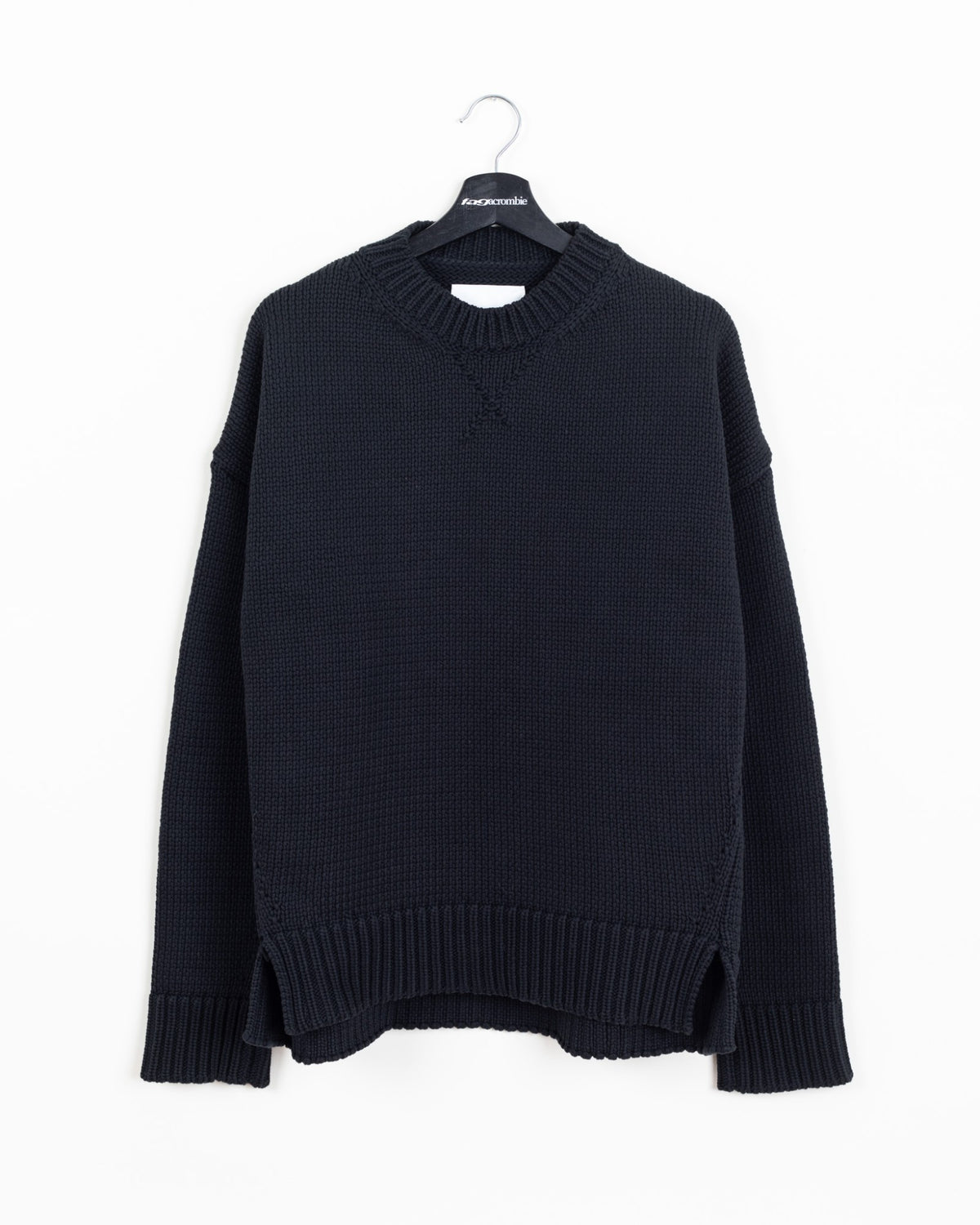 Jil Sander black heavy-knit crewneck sweater, front view on hanger showing ribbed collar, side slits and stepped hem