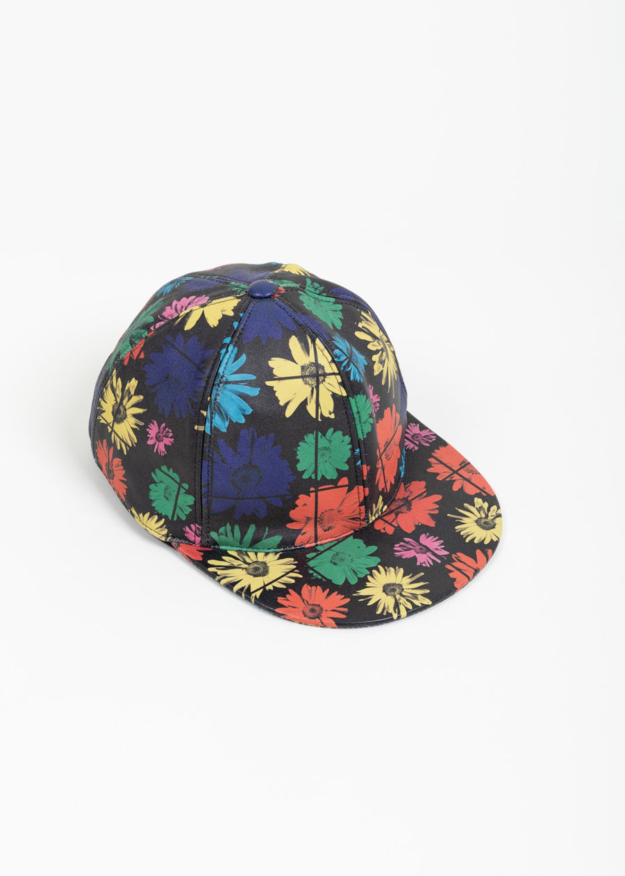 Three-quarter front view of the Moschino black calf leather baseball cap with a multicolor daisy print across the crown and brim