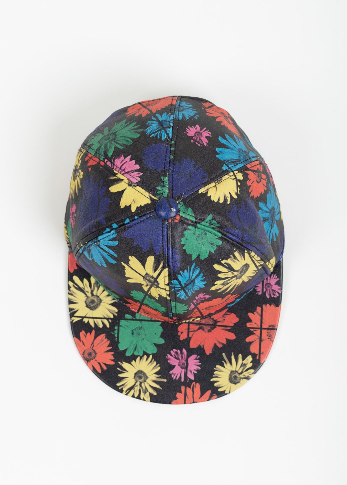Top-down view of the cap showing six printed leather panels meeting at a navy covered button, with the brim below